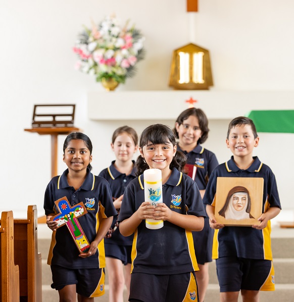 Students standing inside a church holding religious items, with an altar and flowers in the background