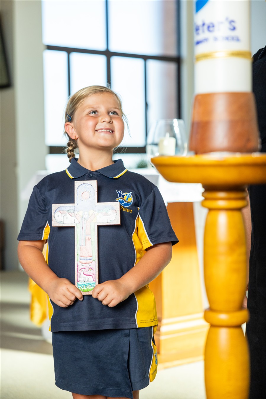 Student holding a cross while teacher lights candle 