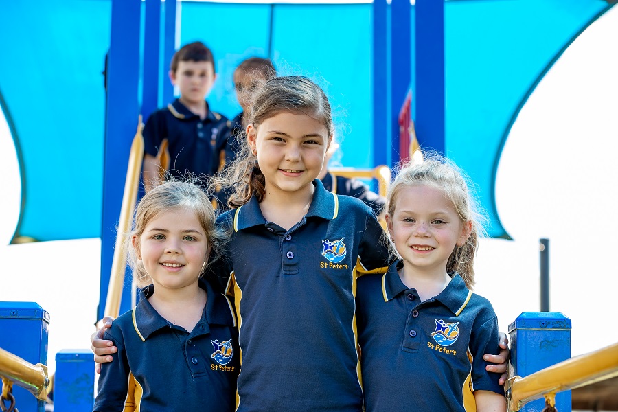 Children in school uniforms standing together on a playground structure under a shade canopy