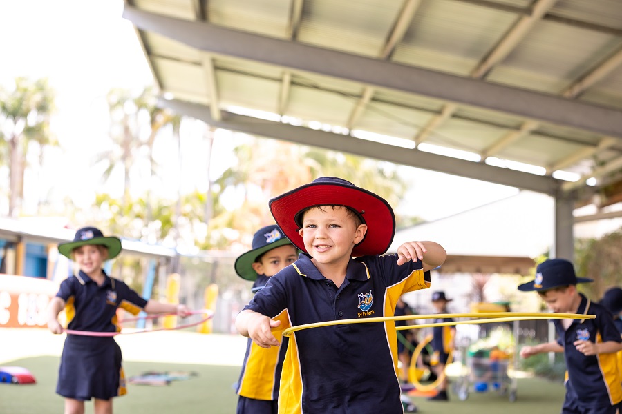 Children in school uniforms using hula hoops in an outdoor covered play area