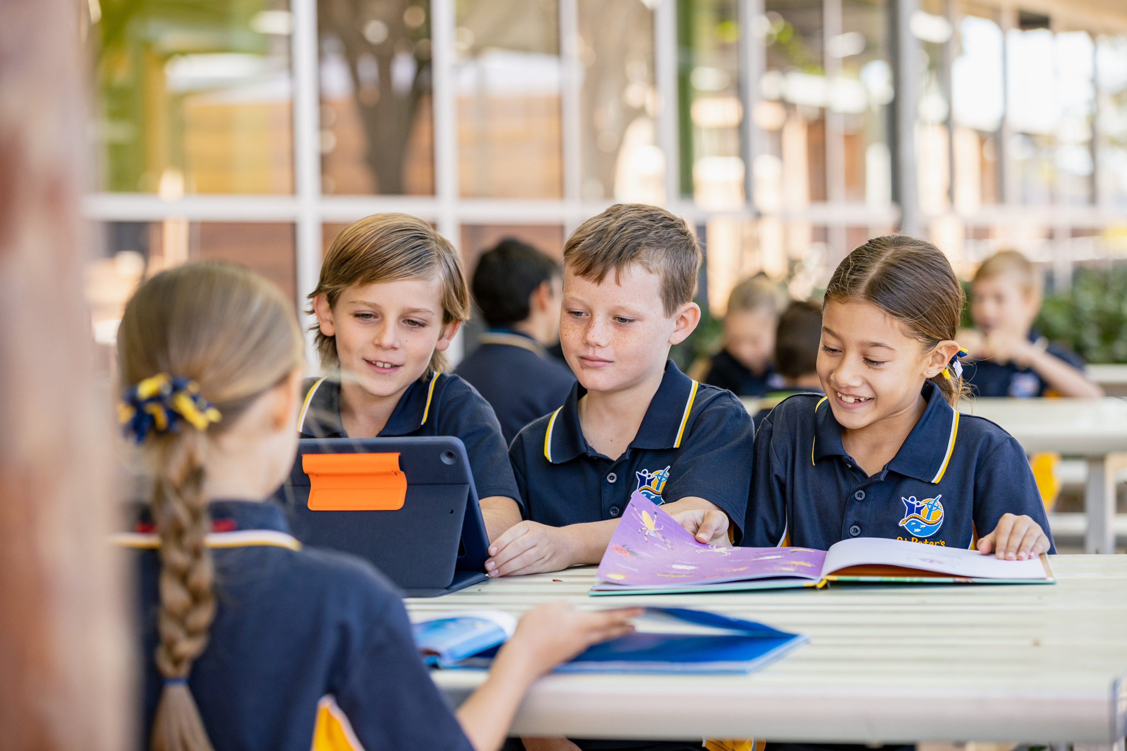 Students sitting at an outdoor table using books and a tablet