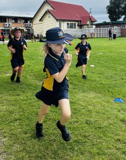 Students in school uniforms running on a grassy field during an outdoor activity